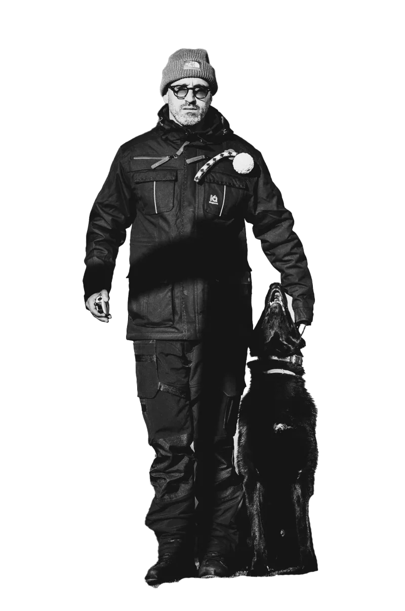 Treinador de pé com um cão preto sentado ao seu lado